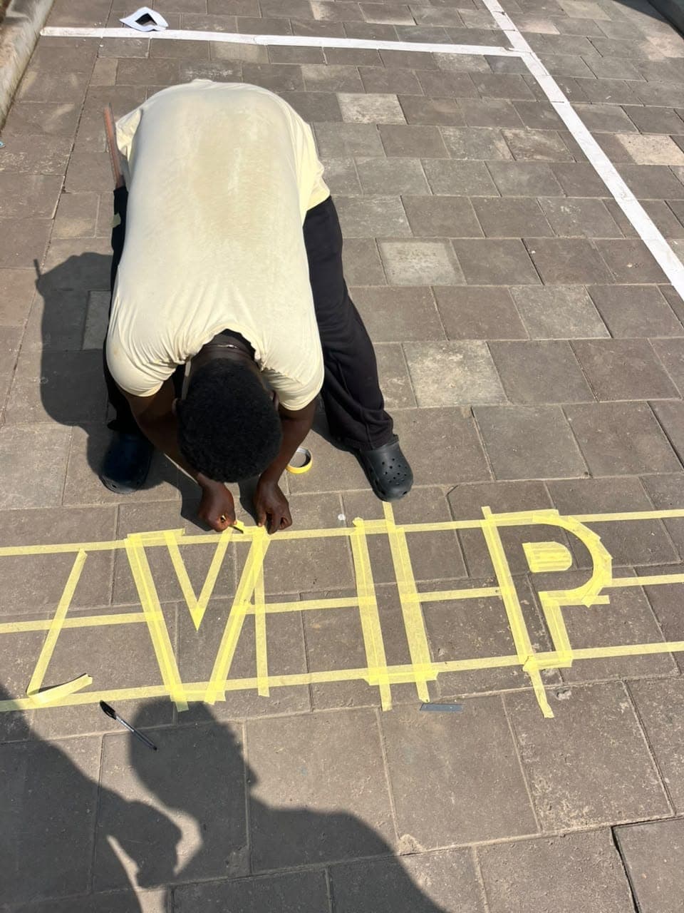 Painter masking custom VIP lettering on a paved parking bay